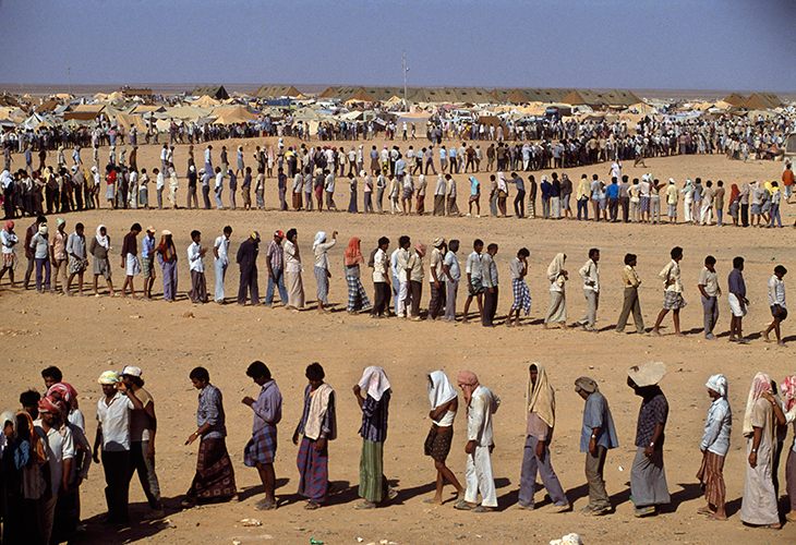 Refugees in the desert. The Sha-alaan One camp, is the worst camp. They have orderly food lines with thousands of refugees waiting calmly for food distribution from the “Charitas” charity organization. Jordan, 1990. © Chris Steele-Perkins / Magnum Photos